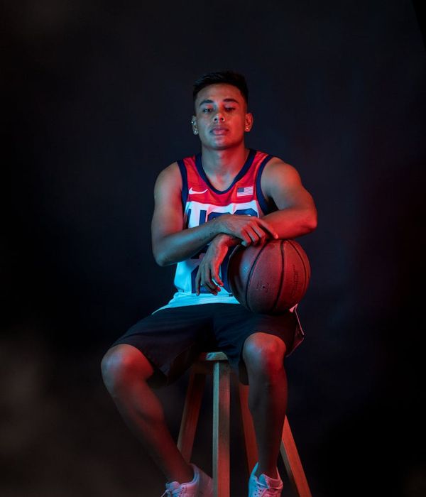 Male athlete in a focused yoga warrior pose in a dark studio.